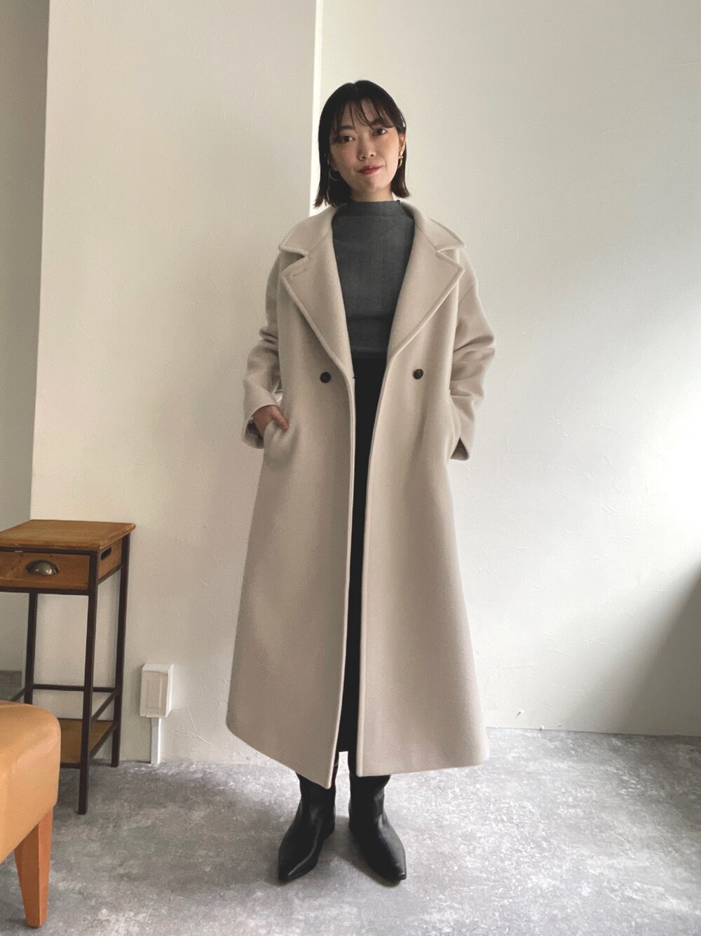 グレー系のニット/セーター、ベージュ系のチェスターコート、ブルー系のワンピースを着用したレディースの秋コーディネートの1枚目の写真