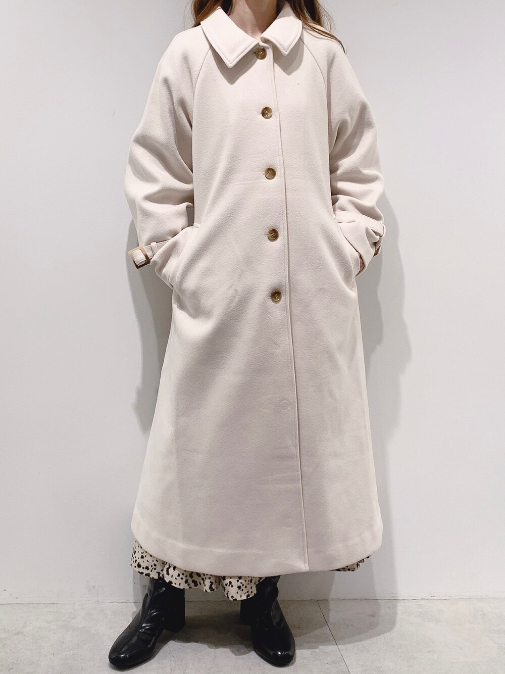 ベージュ系のステンカラーコート、ベージュ系のスカート、ブラック系のブーツを着用したレディースの秋コーディネートの1枚目の写真