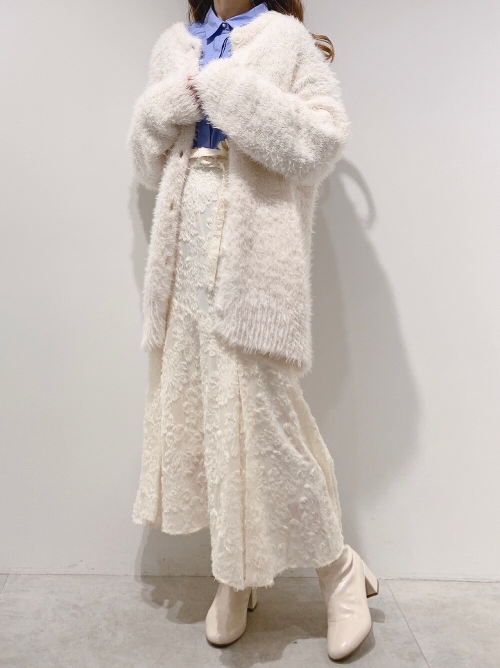 ホワイト系のカーディガン/ボレロ、ホワイト系のスカート、ホワイト系のブーツを着用したレディースの冬コーディネートの1枚目の写真