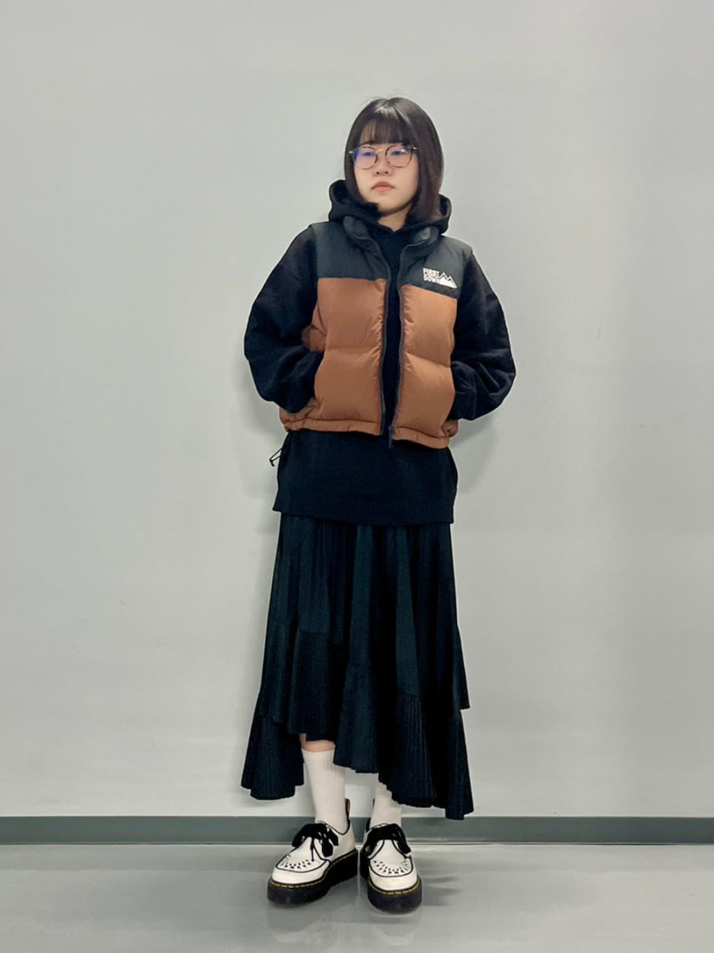 ブラウン系のダウンベスト、ブラック系のパーカーを着用したレディースの秋コーディネートの1枚目の写真