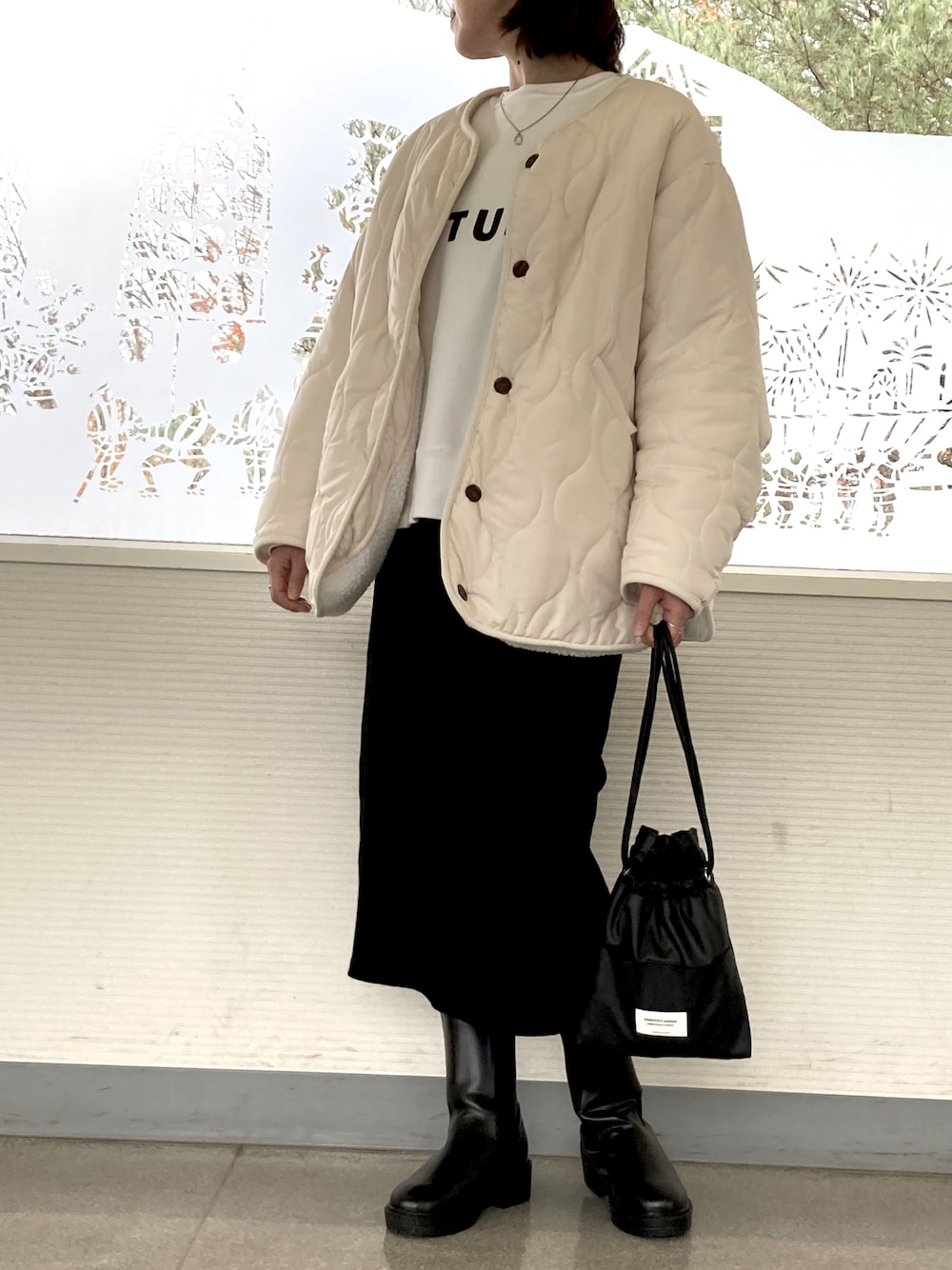 ホワイト系のノーカラージャケット、ブラック系のスカート、ブラック系のショルダーバッグを着用したレディースの秋コーディネートの1枚目の写真