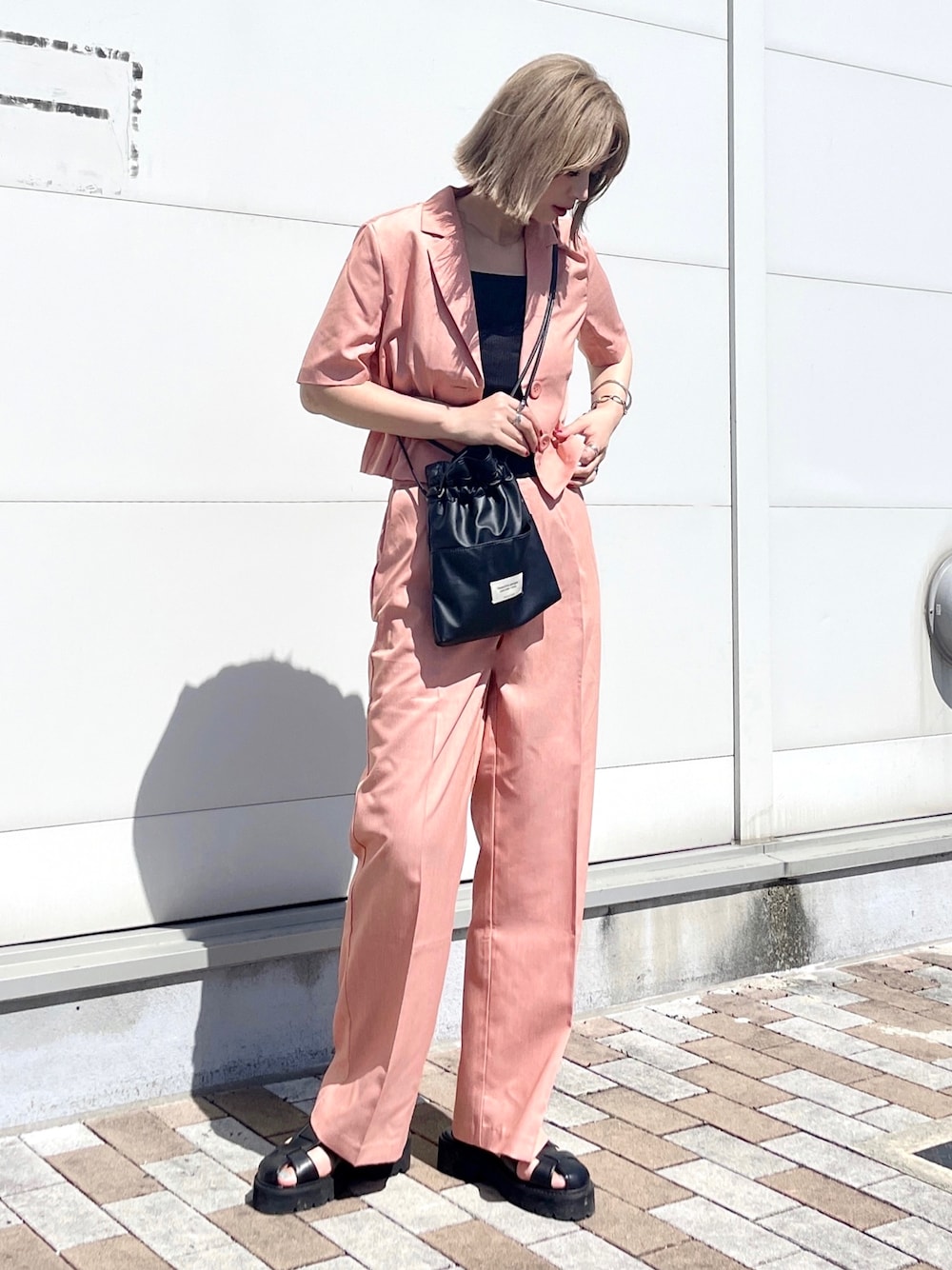 ピンク系のセットアップ、ブラック系のショルダーバッグ、ブラック系のタンクトップを着用したレディースの夏コーディネートの1枚目の写真