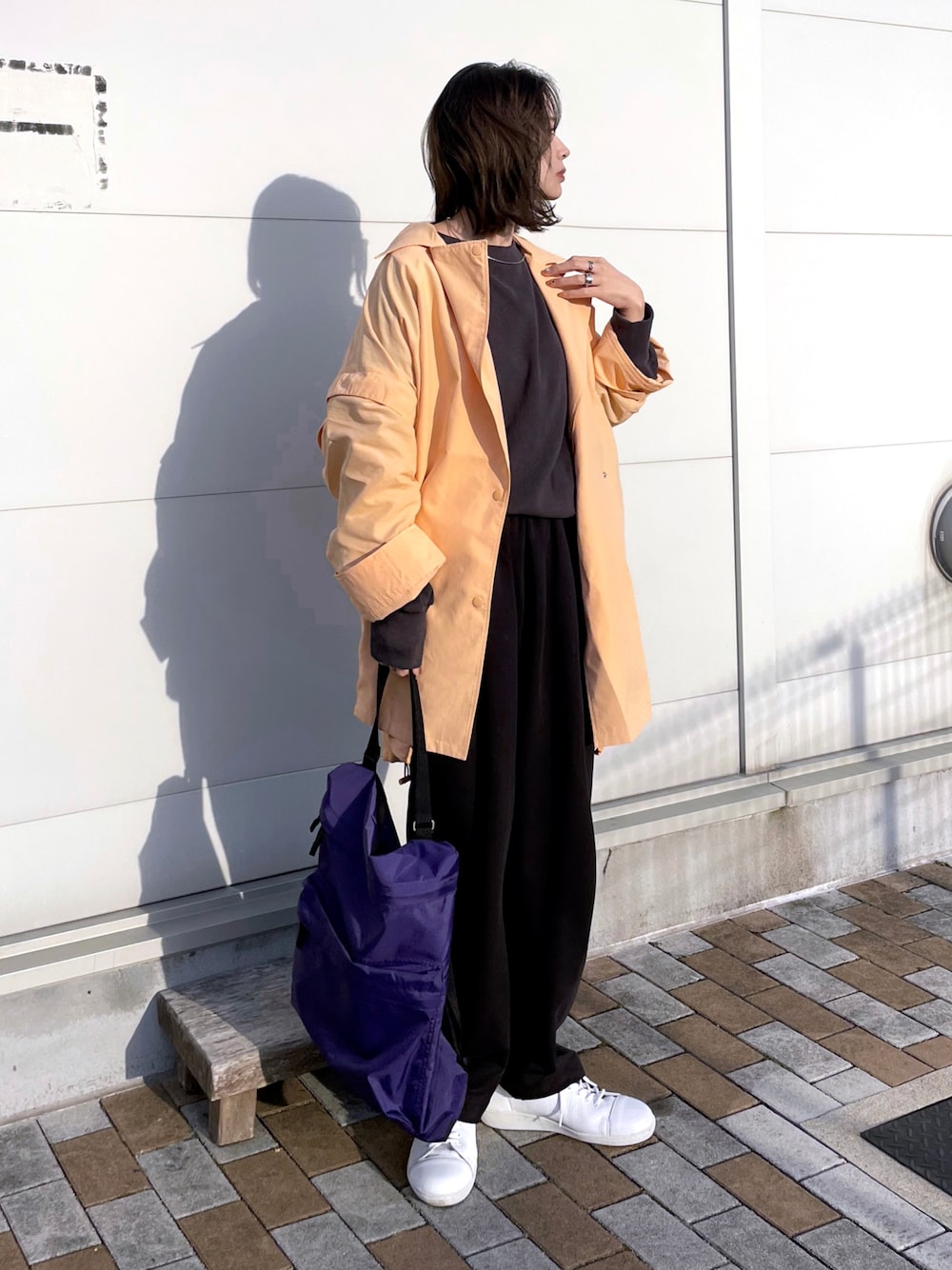 オレンジ系のポンチョ、グレー系のTシャツ/カットソー、ブラック系のパンツを着用したレディースの春コーディネートの1枚目の写真