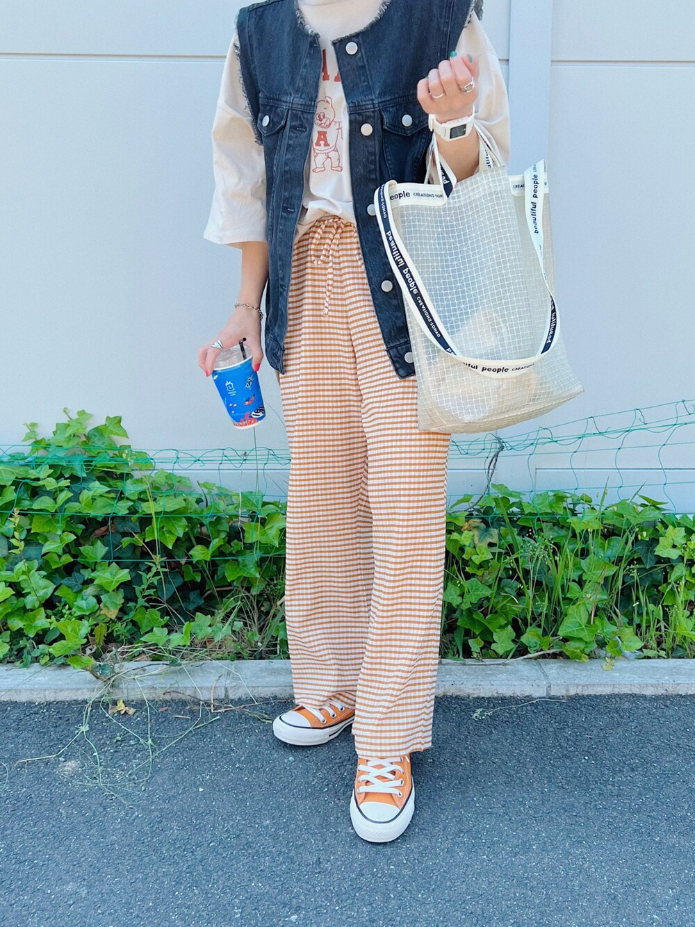 ホワイト系のショルダーバッグ、オレンジ系のスニーカー、ブラック系のベストを着用したレディースの春コーディネートの1枚目の写真