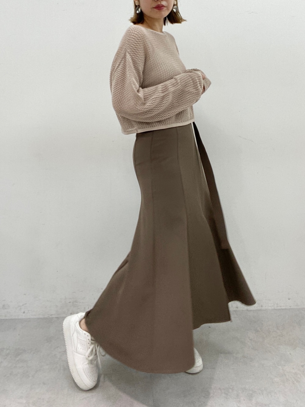 ブラウン系のスカート、ベージュ系のニット/セーター、ホワイト系のスニーカーを着用したレディースの春コーディネートの2枚目の写真
