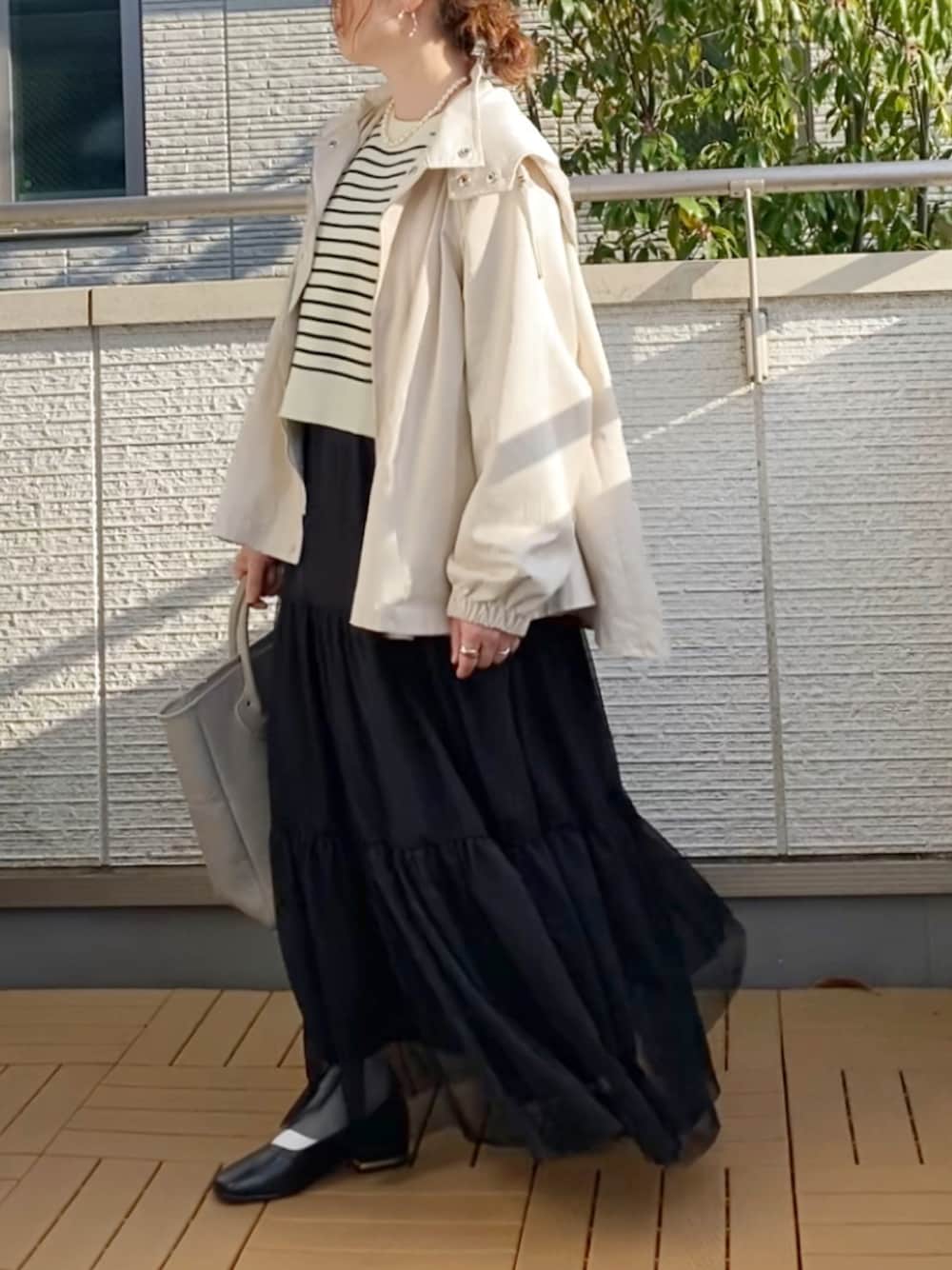 ホワイト系のマウンテンパーカー、ブラック系のカーディガン/ボレロ、ブラック系のスカートを着用したレディースの春コーディネートの1枚目の写真