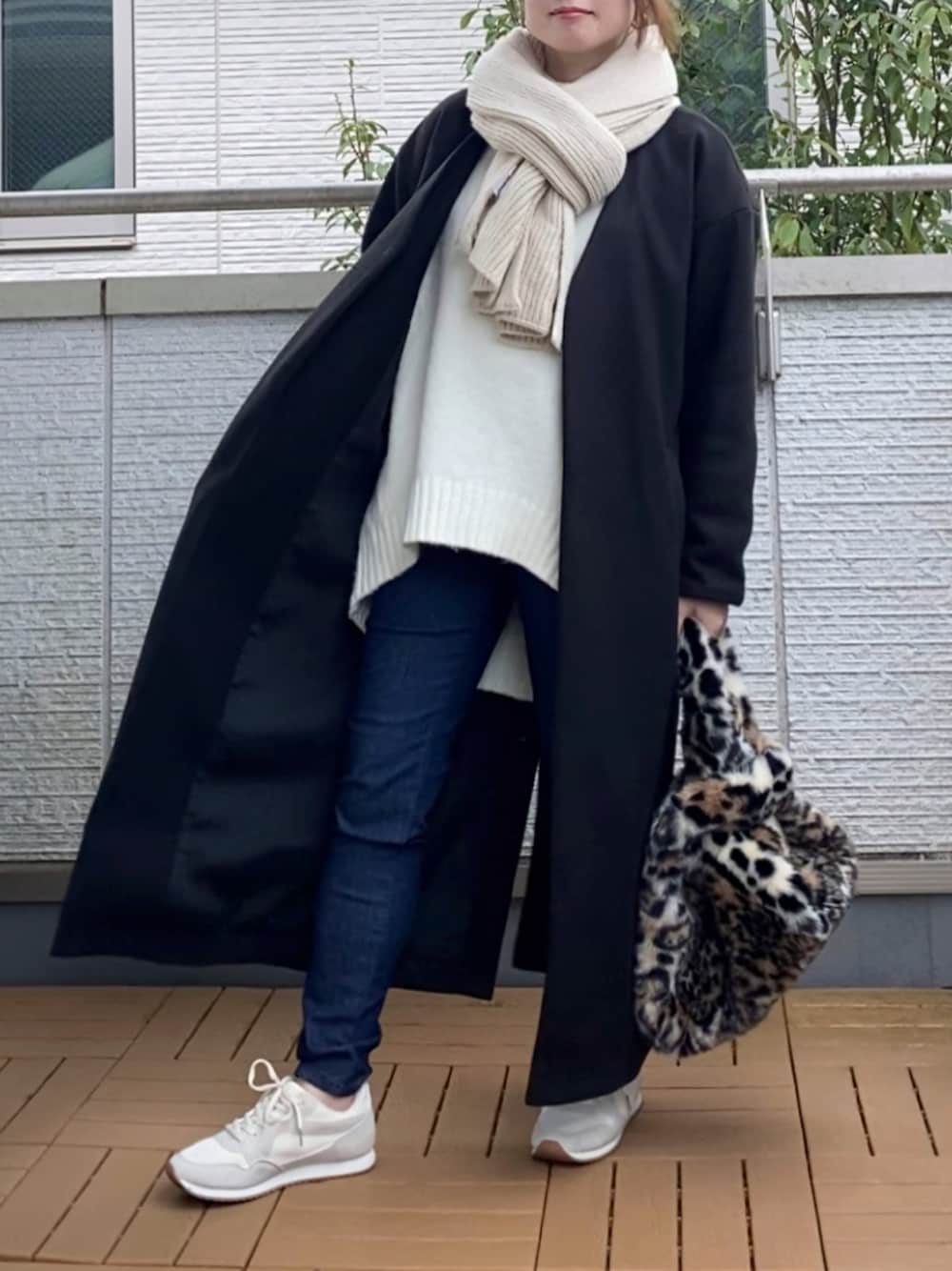 ブラック系のノーカラーコート、ホワイト系のニット/セーター、ブルー系のデニムパンツを着用したレディースの秋コーディネートの1枚目の写真