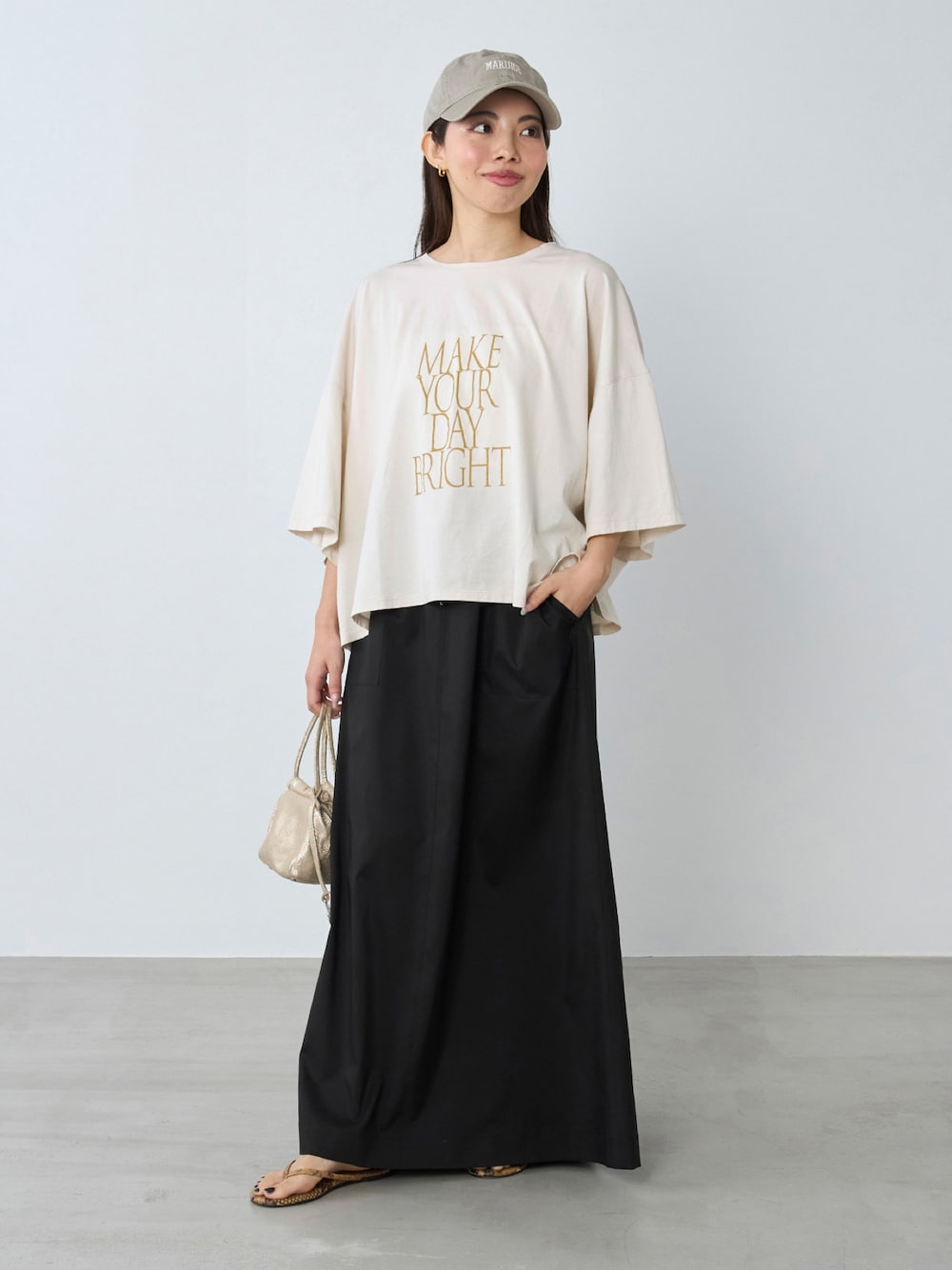 ブラック系のスカート、ベージュ系のTシャツ/カットソーを着用したレディースの夏コーディネートの1枚目の写真