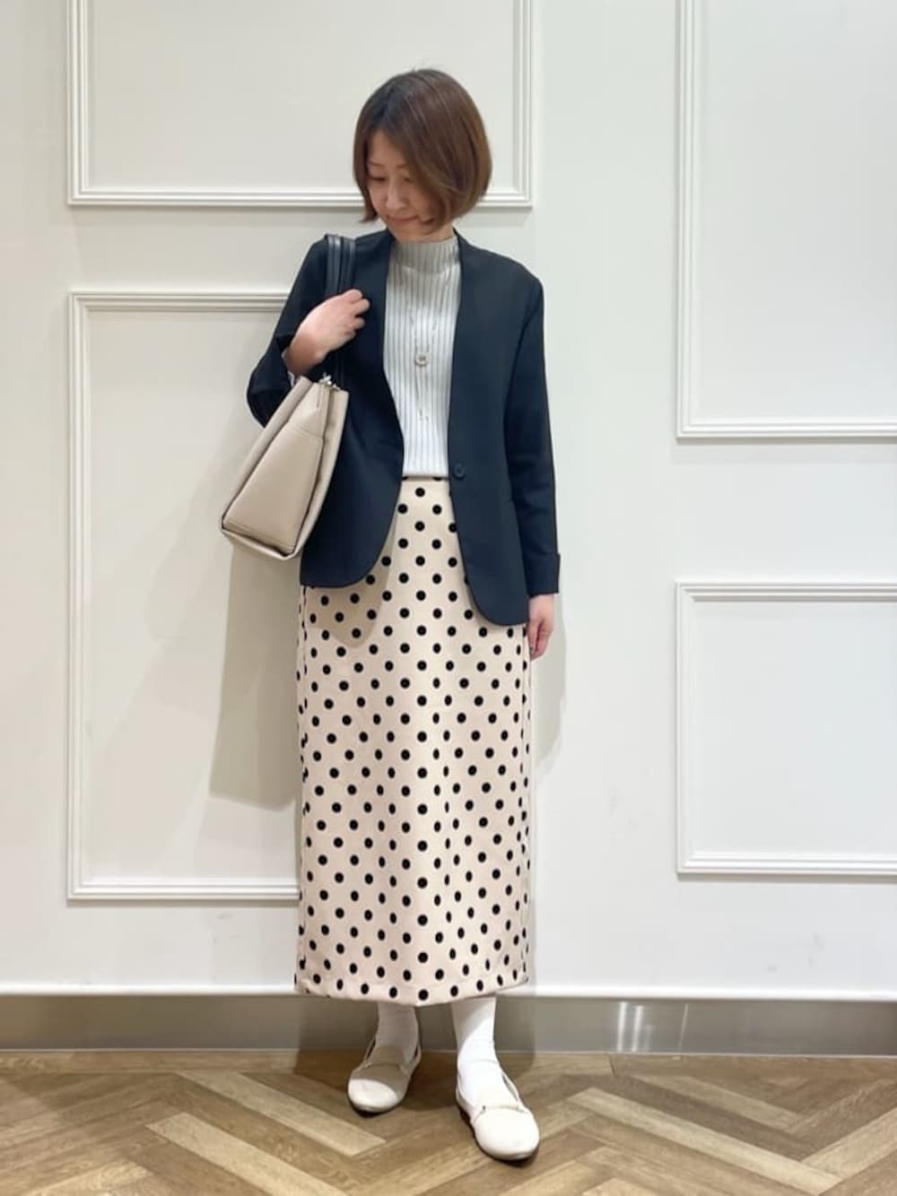 ブラック系のノーカラージャケット、グレー系のニット/セーター、ベージュ系のスカートを着用したレディースの春コーディネートの1枚目の写真