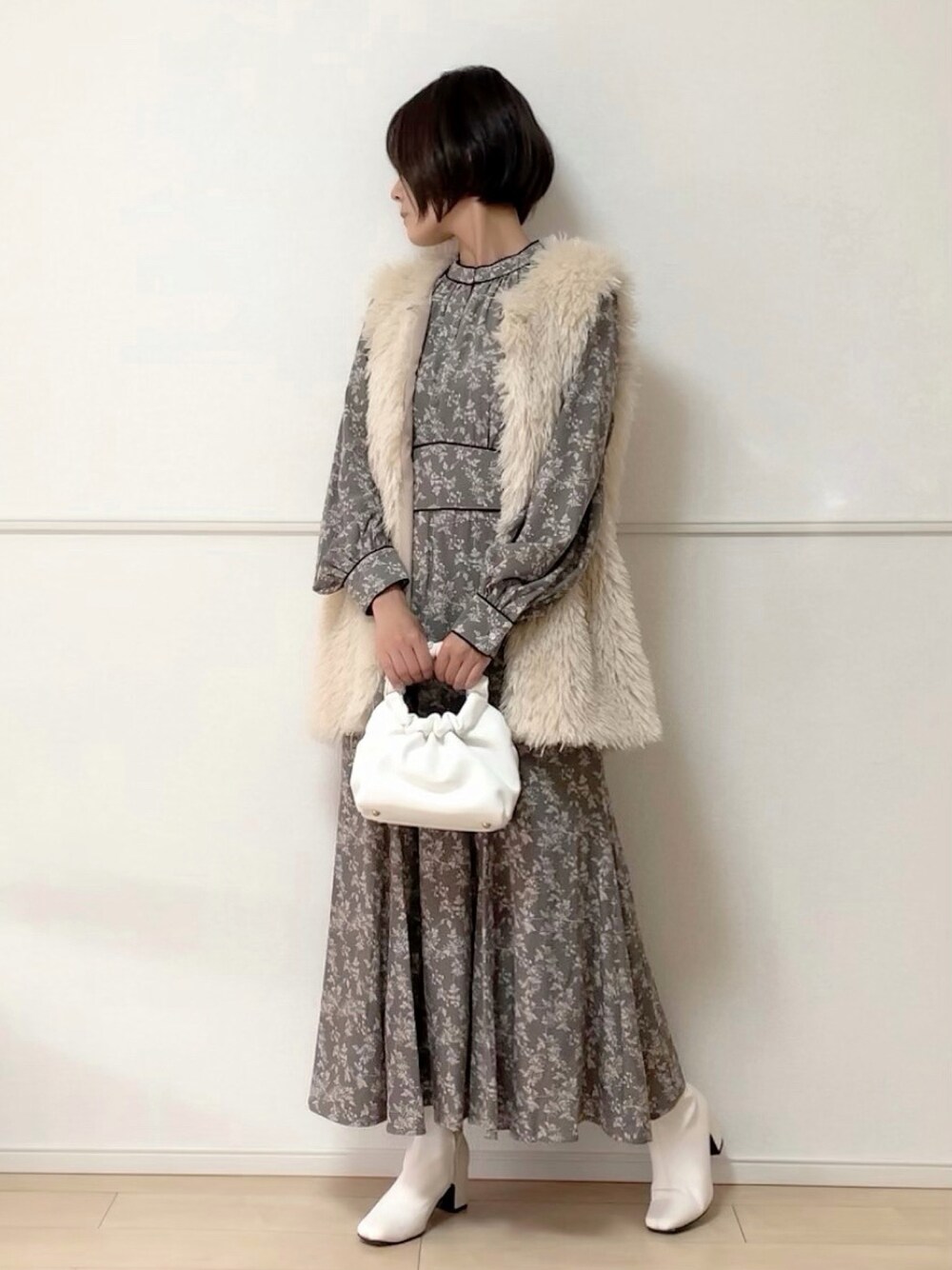 ホワイト系のベスト、グレー系のワンピース、ホワイト系のブーツを着用したレディースの秋コーディネートの1枚目の写真