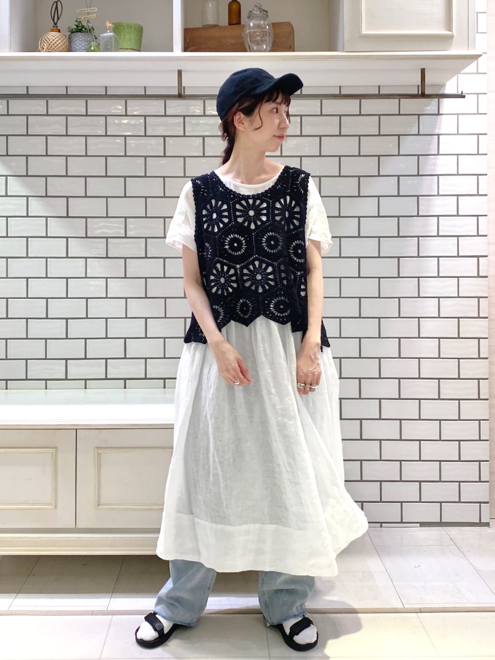 ブラック系のベスト、ホワイト系のワンピース、ブルー系のデニムパンツを着用したレディースの夏コーディネートの2枚目の写真