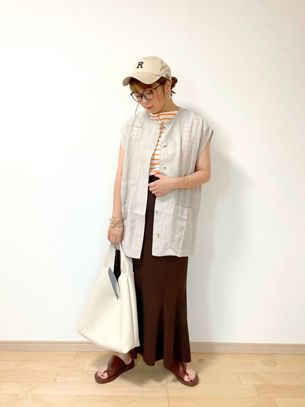 グレー系のベスト、オレンジ系のTシャツ/カットソー、ブラウン系のスカートを着用したレディースの夏コーディネートの1枚目の写真