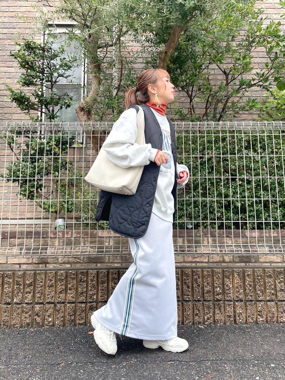 ベージュ系のスウェット、オレンジ系のトップス、グレー系のスカートを着用したレディースの冬コーディネートの1枚目の写真