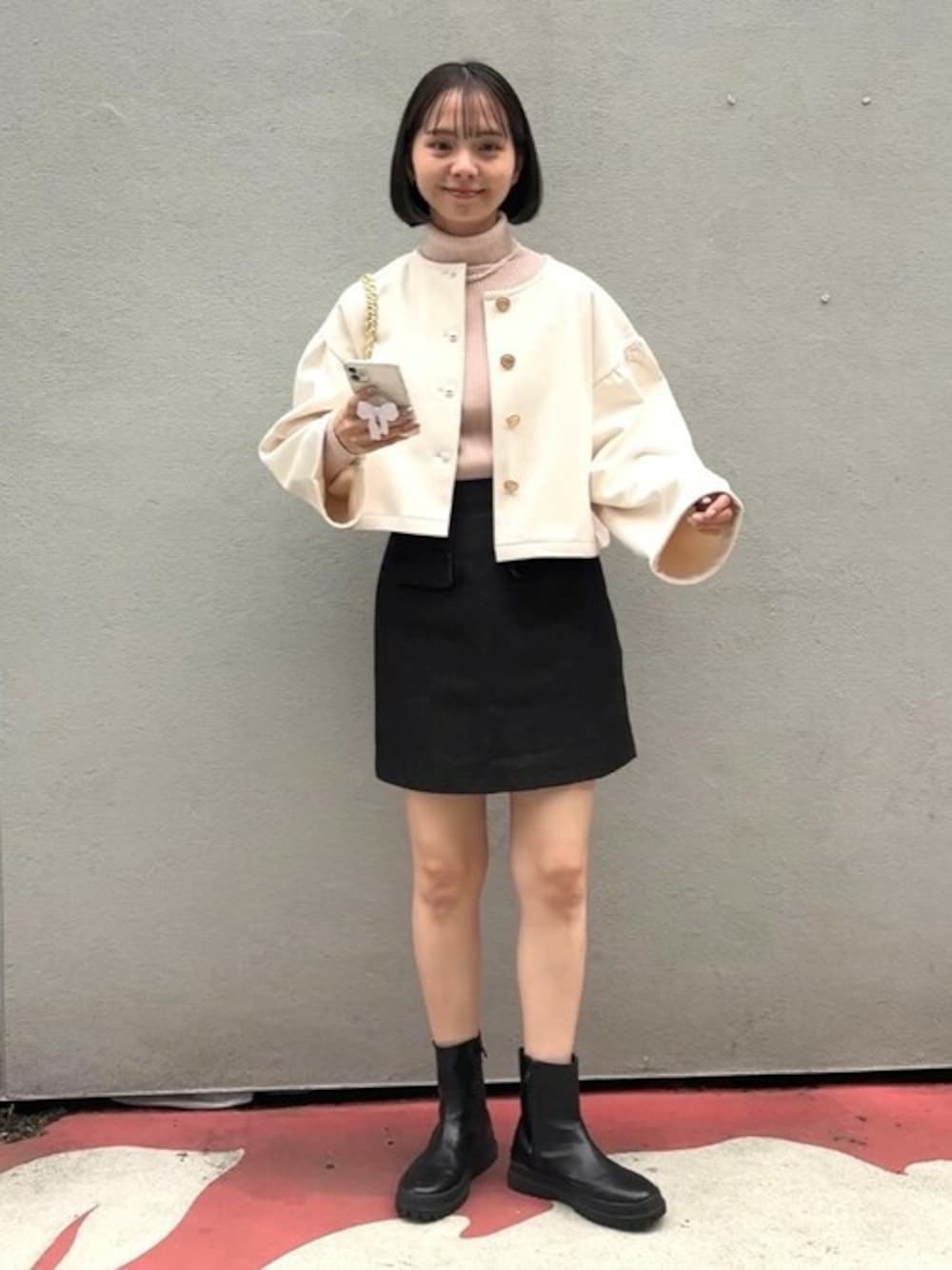 ブラック系のデニムスカート、ホワイト系のノーカラージャケット、ピンク系のニット/セーターを着用したレディースの春コーディネートの1枚目の写真