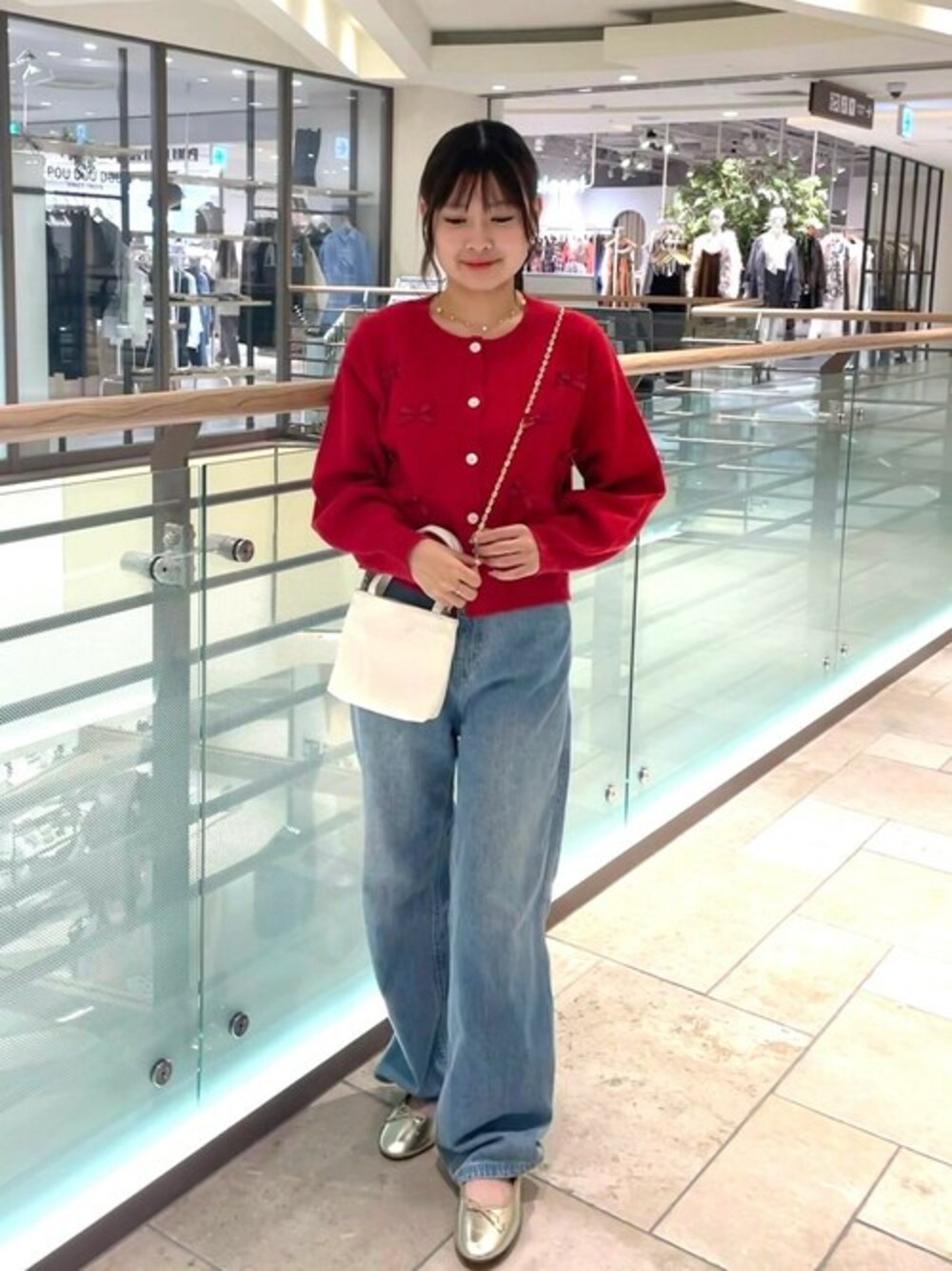 レッド系のニット/セーター、ブルー系のデニムパンツ、ホワイト系のショルダーバッグを着用したレディースの秋コーディネートの1枚目の写真