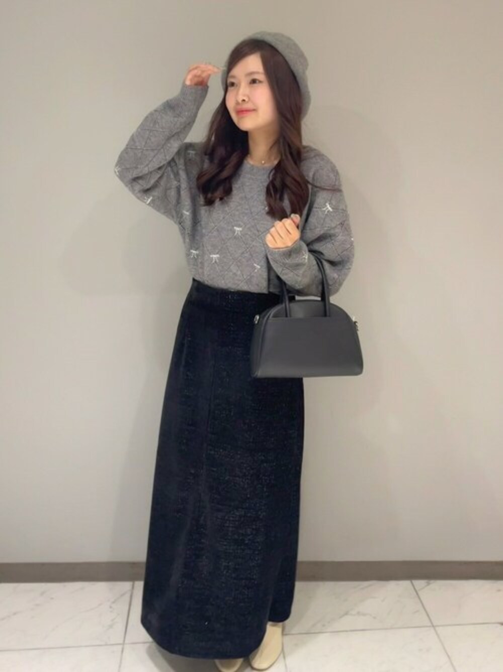 グレー系のニット/セーター、ブラック系のスカート、ブラック系のハンドバッグを着用したレディースの秋コーディネートの1枚目の写真