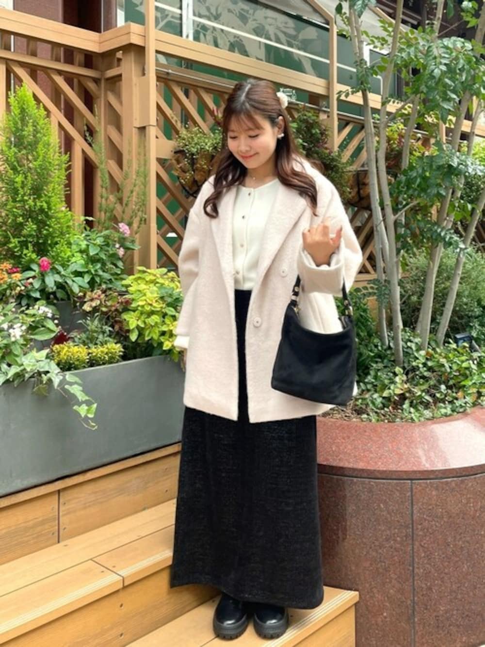 ブラック系のショルダーバッグ、ベージュ系のチェスターコート、ブラック系のスカートを着用したレディースの秋コーディネートの1枚目の写真