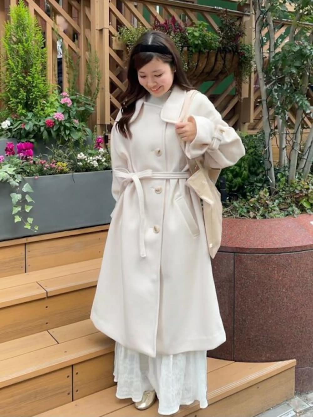 ホワイト系のステンカラーコート、ホワイト系のスカート、ブラック系のカチューシャを着用したレディースの冬コーディネートの1枚目の写真