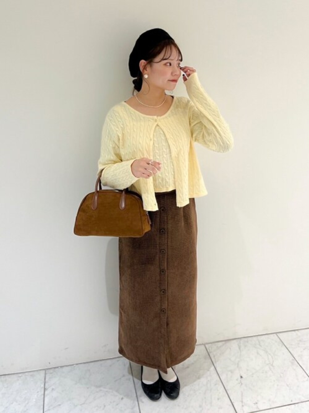 ブラウン系のスカート、ブラウン系のハンドバッグ、ホワイト系のニット/セーターを着用したレディースの冬コーディネートの1枚目の写真