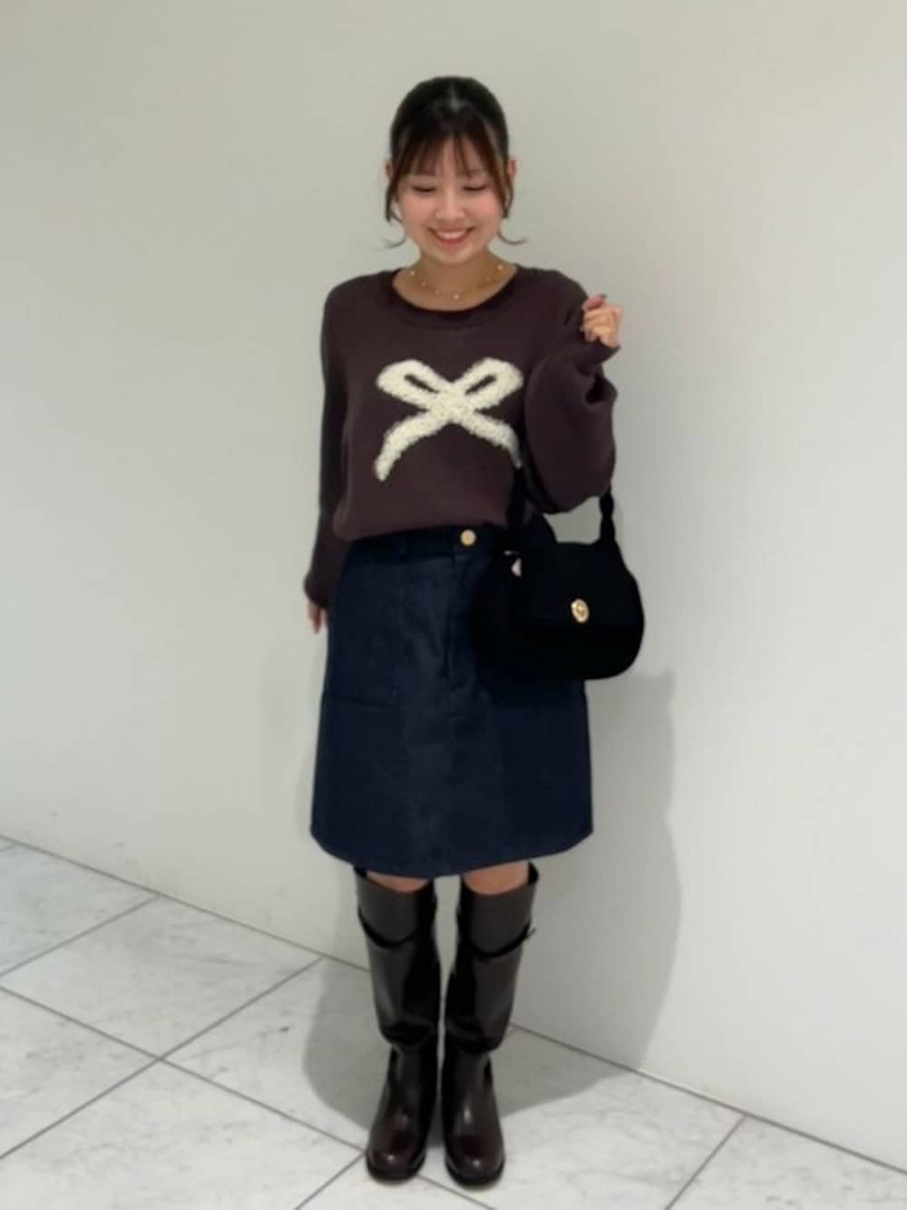 ブラウン系のニット/セーター、ブルー系のデニムスカート、ブラック系のショルダーバッグを着用したレディースの冬コーディネートの1枚目の写真