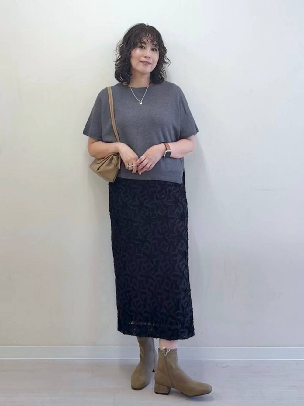 グレー系のニット/セーター、ベージュ系のショルダーバッグ、ブラック系のスカートを着用したレディースの夏コーディネートの1枚目の写真