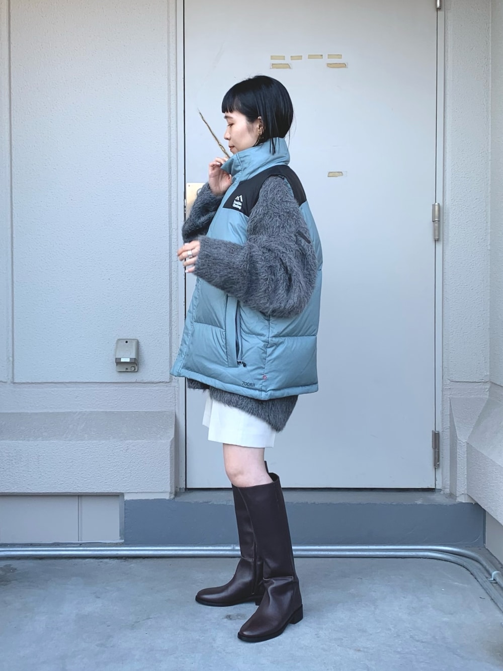 グレー系のニット/セーター、ブルー系のダウンベスト、ブラウン系のブーツを着用したレディースの秋コーディネートの1枚目の写真