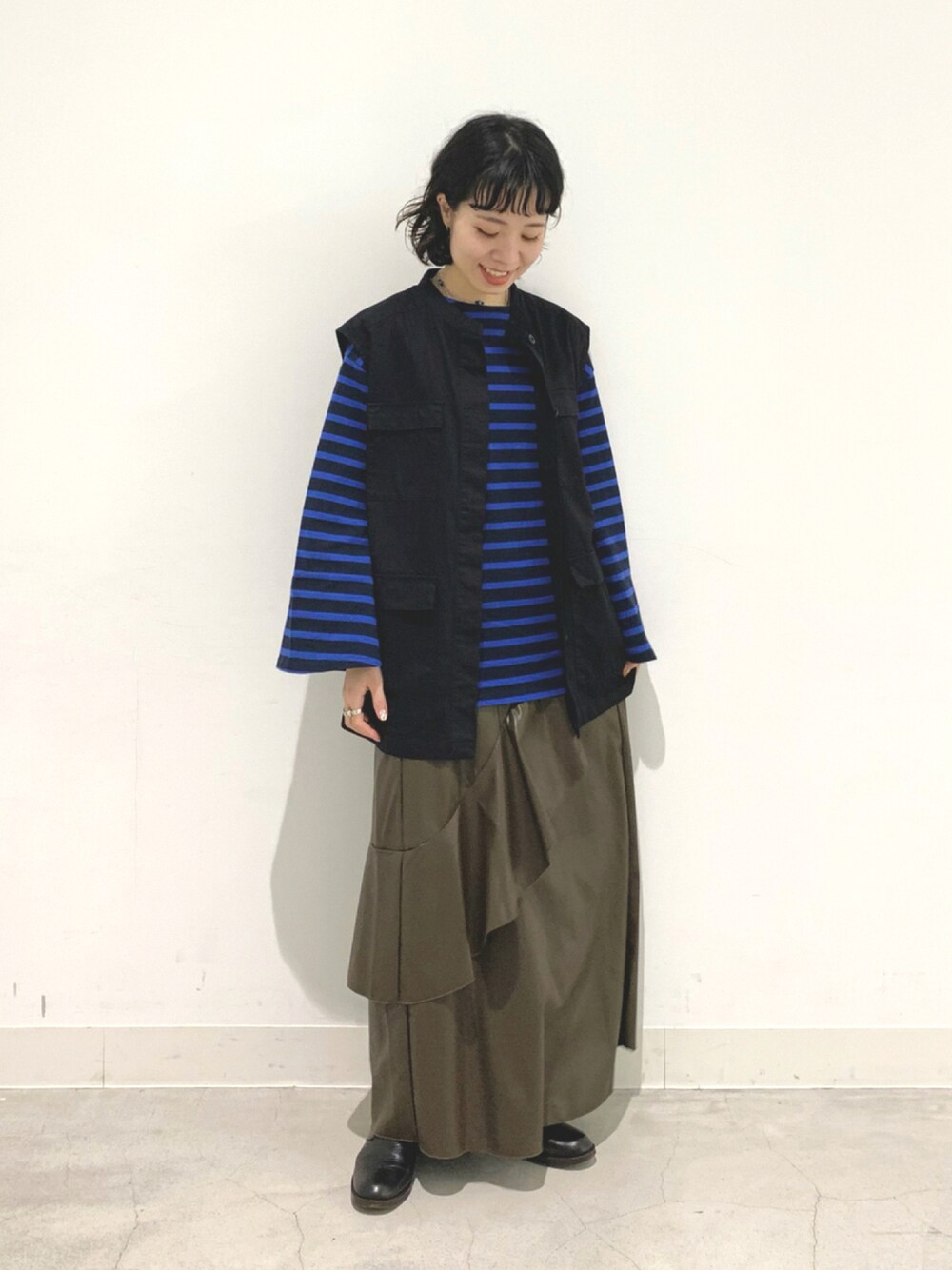 ブルー系のTシャツ/カットソー、ブラック系のベスト、ブラウン系のスカートを着用したレディースの秋コーディネートの1枚目の写真
