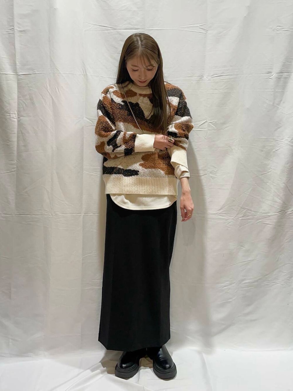 ホワイト系のニット/セーター、ブラック系のスカート、ホワイト系のTシャツ/カットソーを着用したレディースの冬コーディネートの1枚目の写真