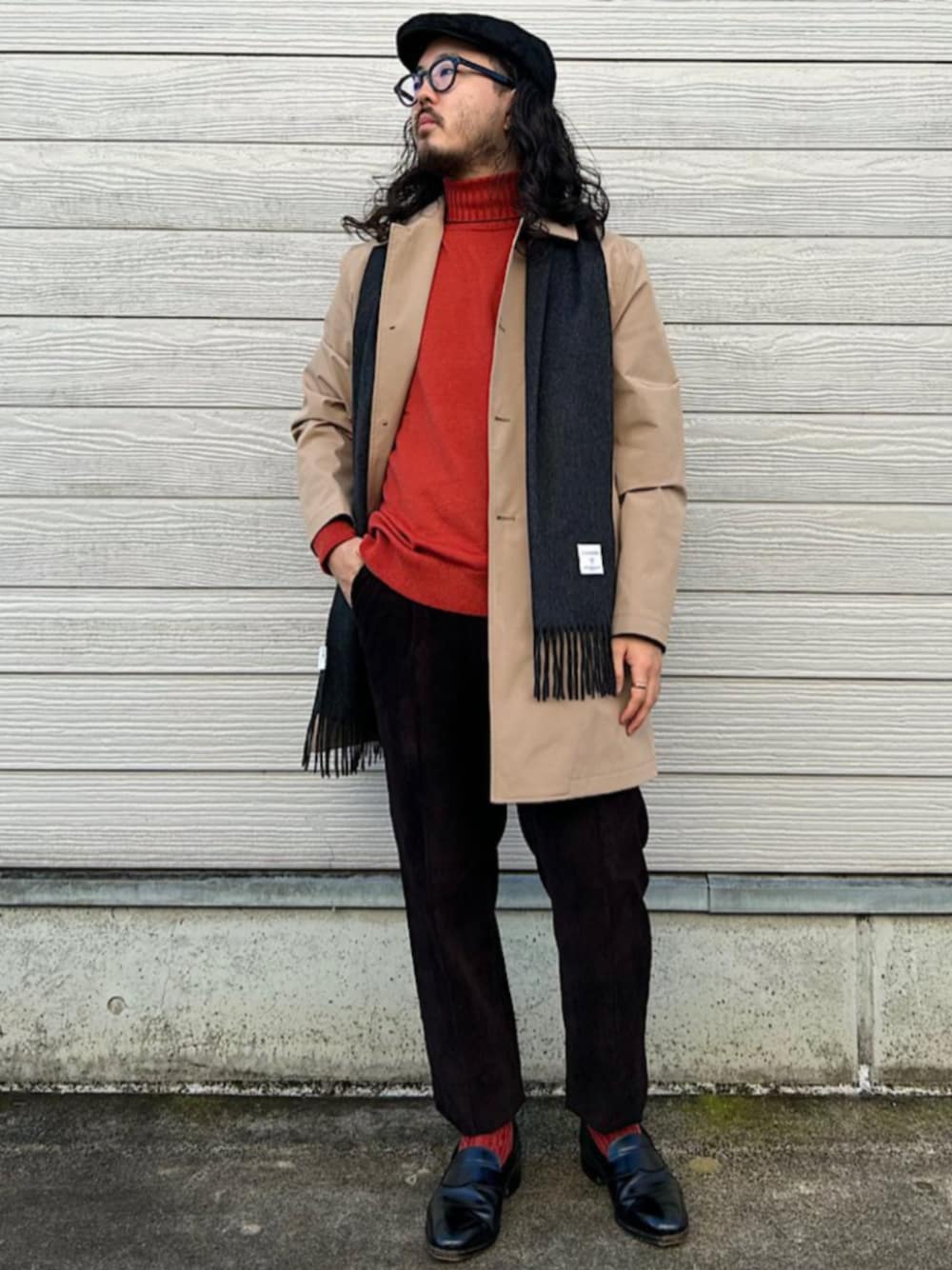 ベージュ系のステンカラーコート、オレンジ系のニット/セーター、グレー系のマフラーを着用したメンズの秋コーディネートの1枚目の写真