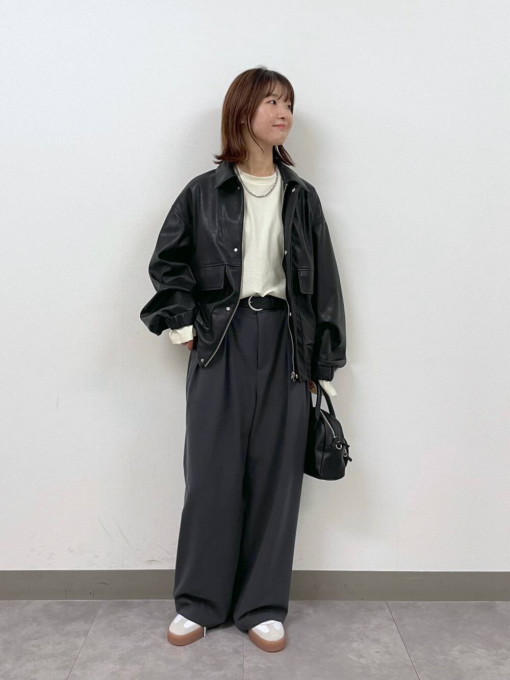 ブラック系のブルゾン、ブラック系のショルダーバッグ、グレー系のスラックスを着用したレディースの秋コーディネートの1枚目の写真