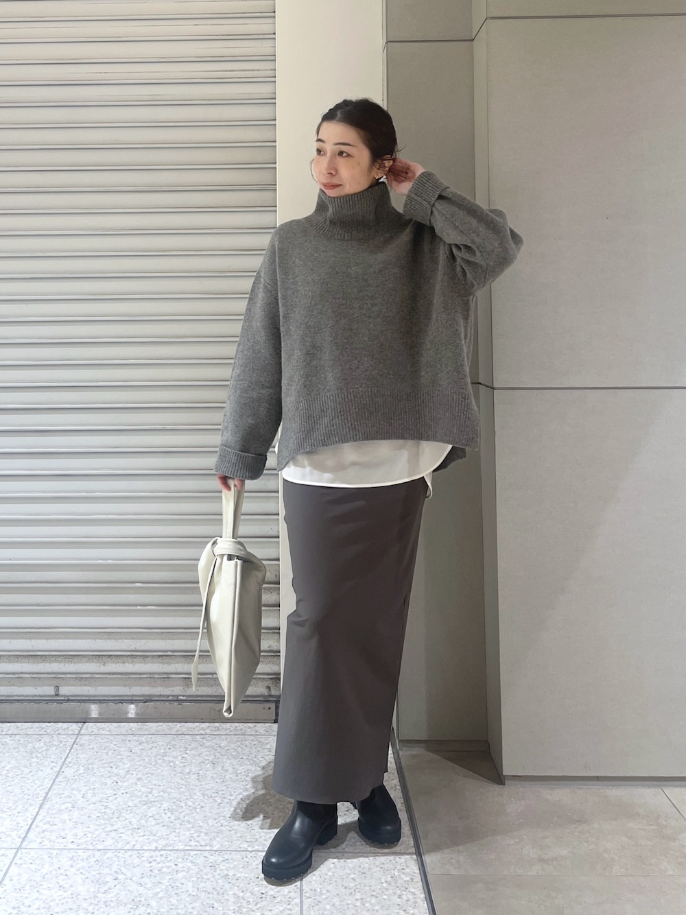 グレー系のニット/セーター、ホワイト系のシャツ/ブラウス、グレー系のスカートを着用したレディースの秋コーディネートの1枚目の写真