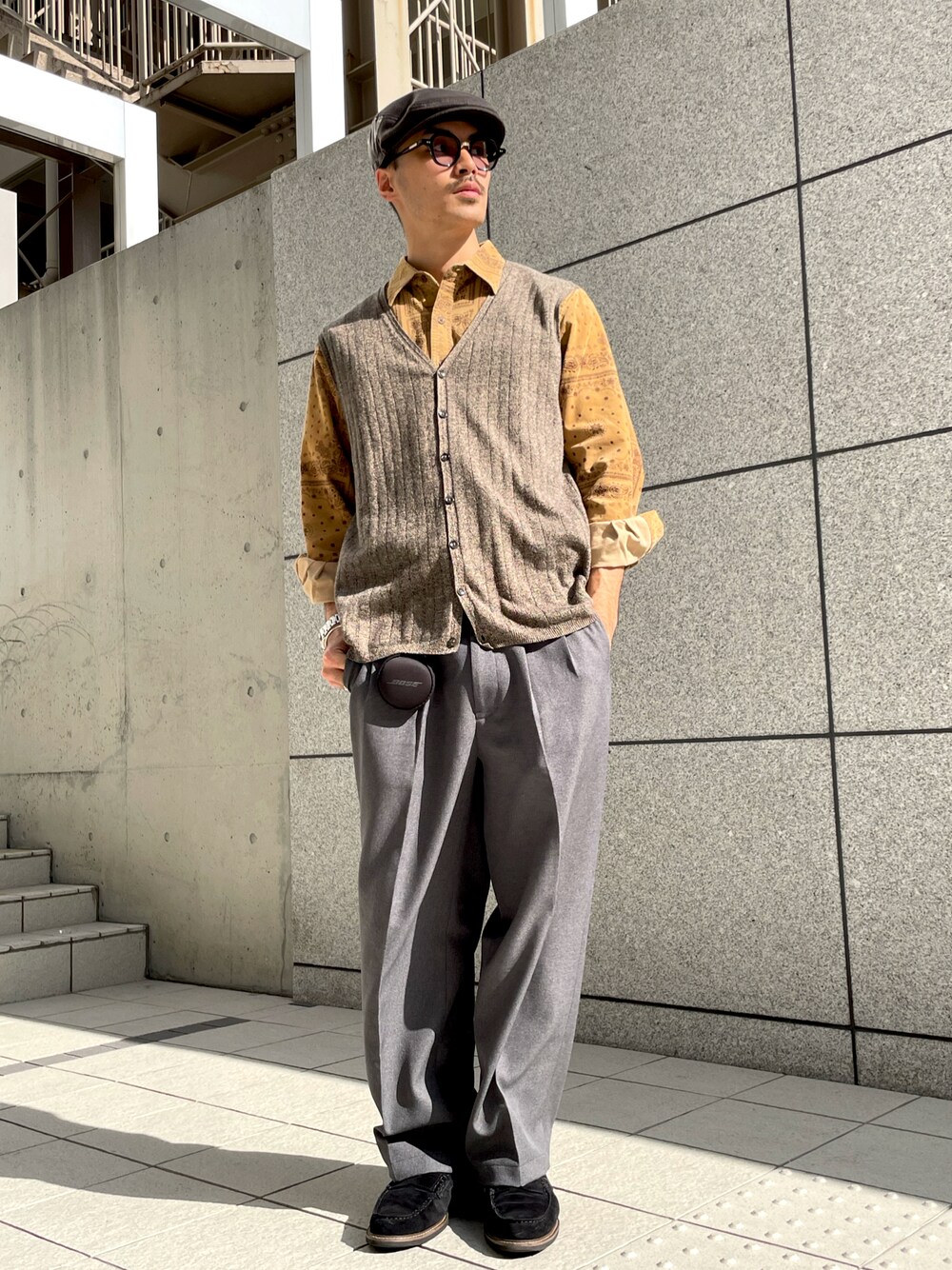 グレー系のスラックス、ベージュ系のベスト、ブラック系のローファーを着用したメンズの秋コーディネートの1枚目の写真
