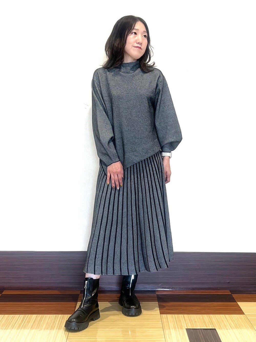 ブラック系のニット/セーター、ブラック系のスカート、ブラック系のブーツを着用したレディースの秋コーディネートの1枚目の写真