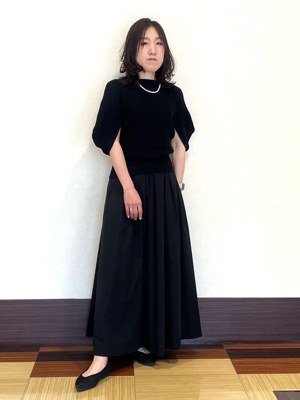 ブラック系のニット/セーター、ブラック系のスカート、ブラック系のパンプスを着用したレディースの夏コーディネートの1枚目の写真