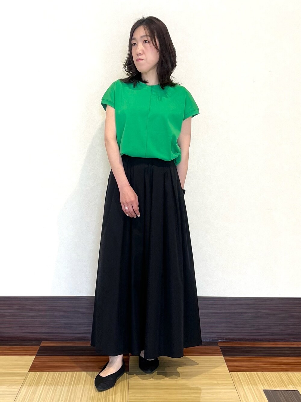 グリーン系のTシャツ/カットソー、ブラック系のスカート、ブラック系のパンプスを着用したレディースの夏コーディネートの1枚目の写真
