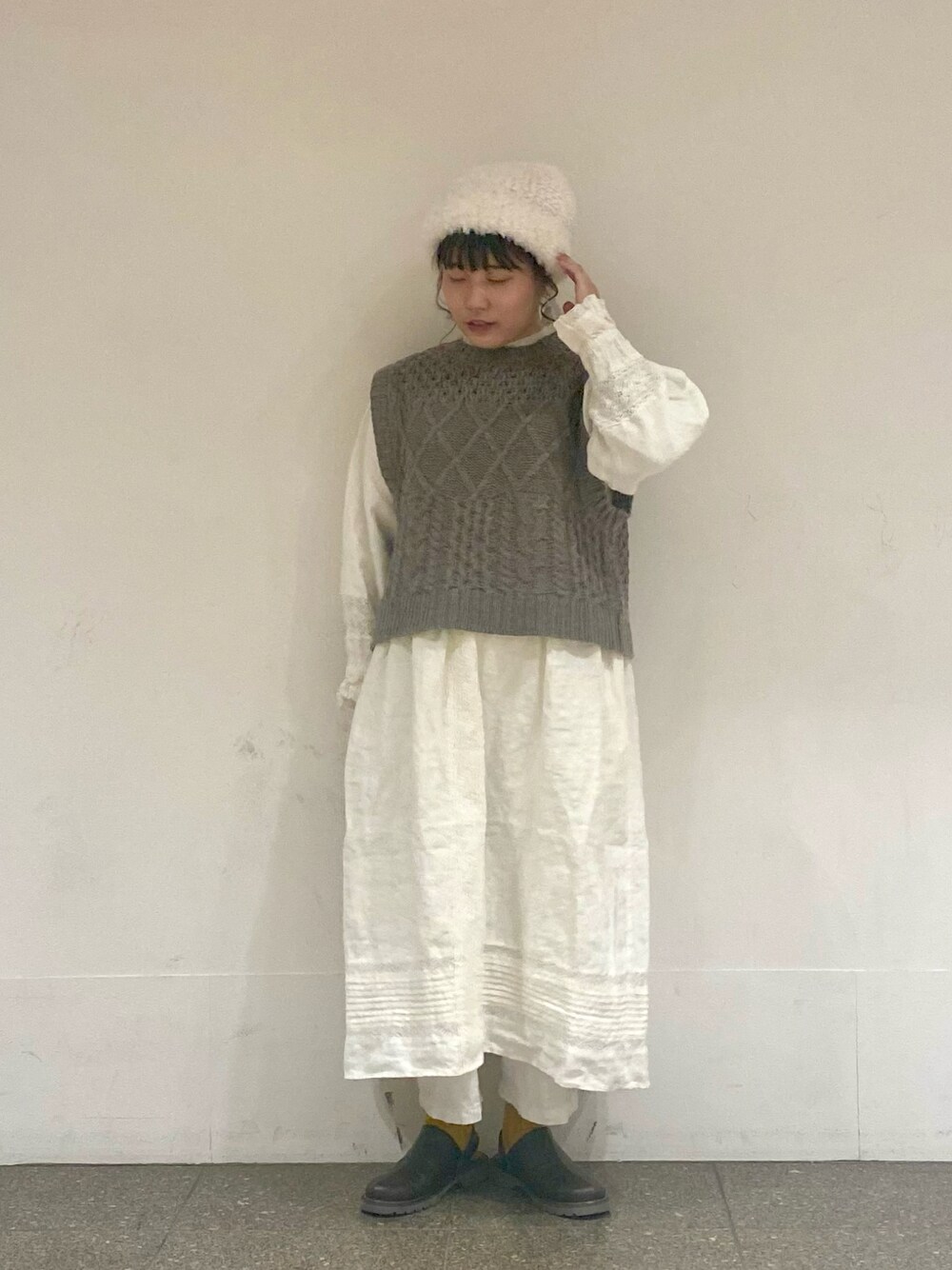 ブラウン系のベスト、ホワイト系のワンピース、ホワイト系のイヤリングを着用したレディースの冬コーディネートの1枚目の写真