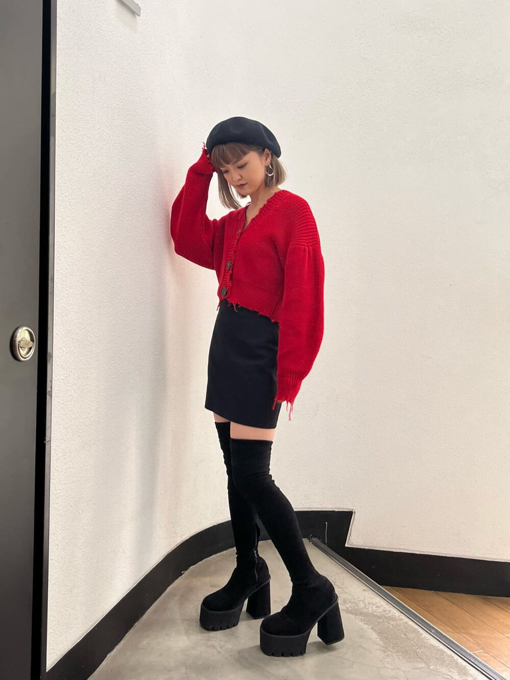 ブラック系のスカート、レッド系のカーディガン/ボレロ、ブラック系のブーツを着用したレディースの秋コーディネートの1枚目の写真