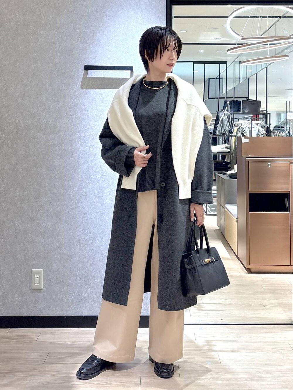 ブラック系のショルダーバッグ、ホワイト系のニット/セーター、グレー系のチェスターコートを着用したレディースの秋コーディネートの1枚目の写真