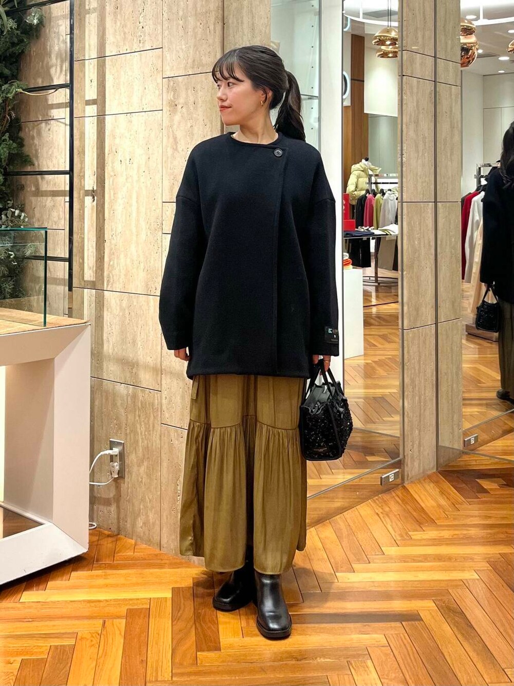 イエロー系のワンピース、ブラック系のその他アウター、ブラック系のハンドバッグを着用したレディースの冬コーディネートの1枚目の写真