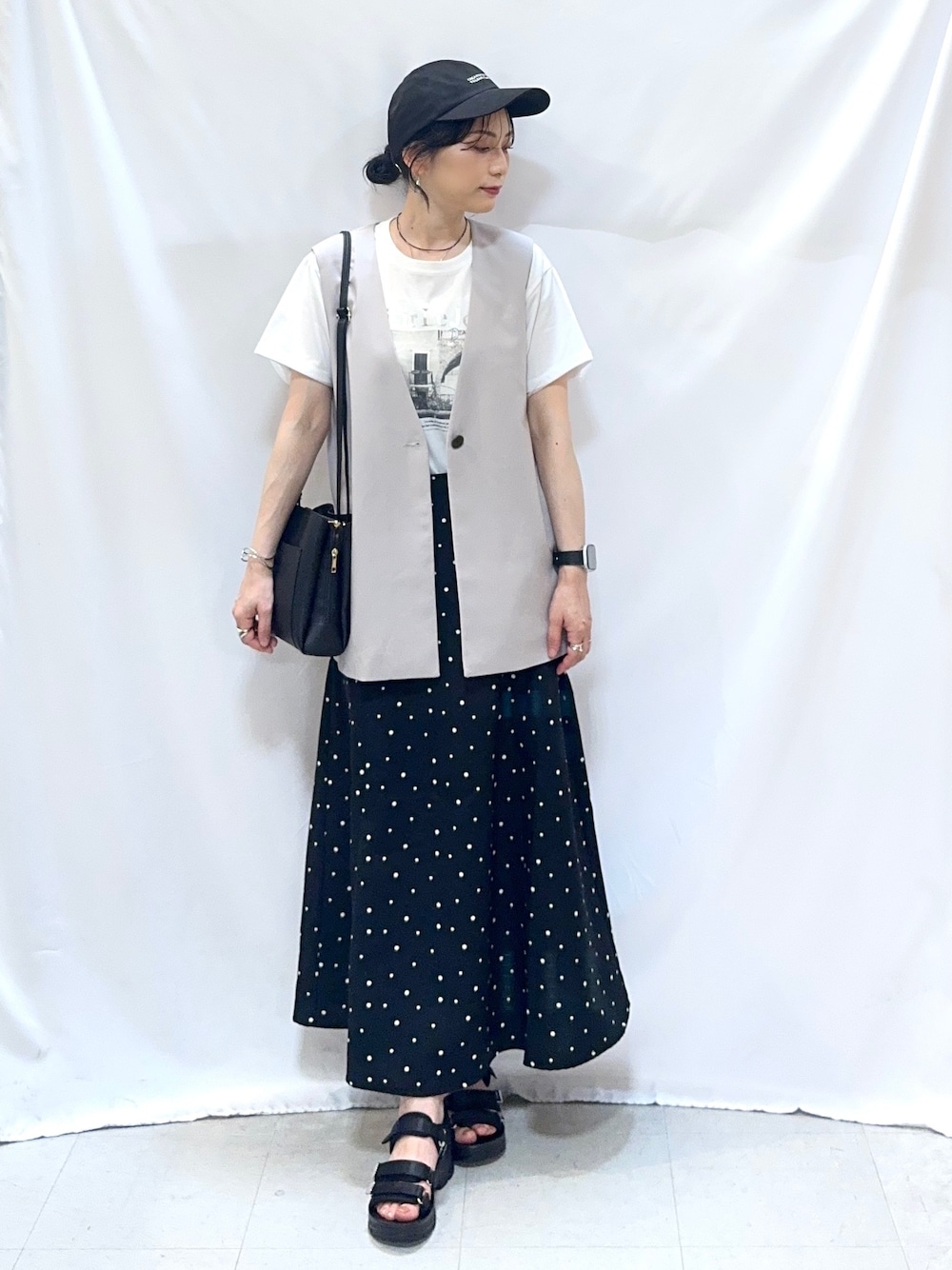 ベージュ系のベスト、ホワイト系のTシャツ/カットソー、ブラック系のスカートを着用したレディースの夏コーディネートの1枚目の写真