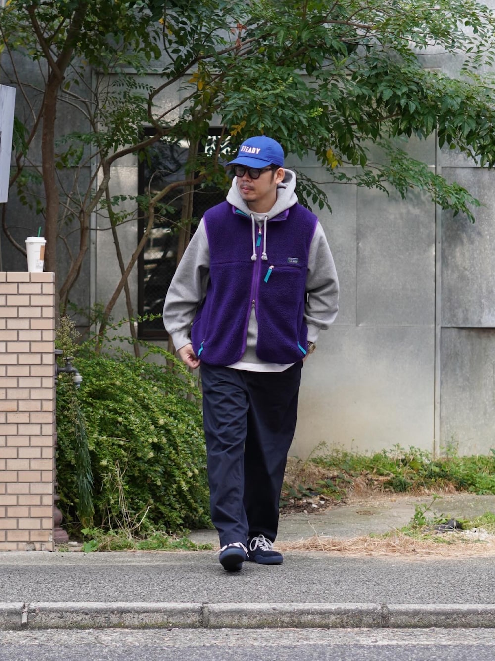 パープル系のベスト、グレー系のパーカー、ブルー系のチノパンツを着用したメンズの秋コーディネートの1枚目の写真