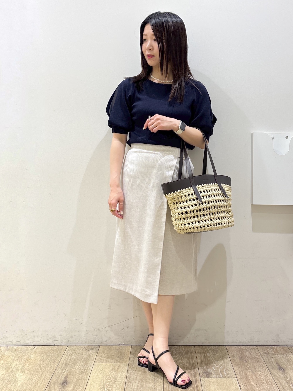 ブルー系のニット/セーター、ベージュ系のスカート、ブラウン系のトートバッグを着用したレディースの夏コーディネートの1枚目の写真
