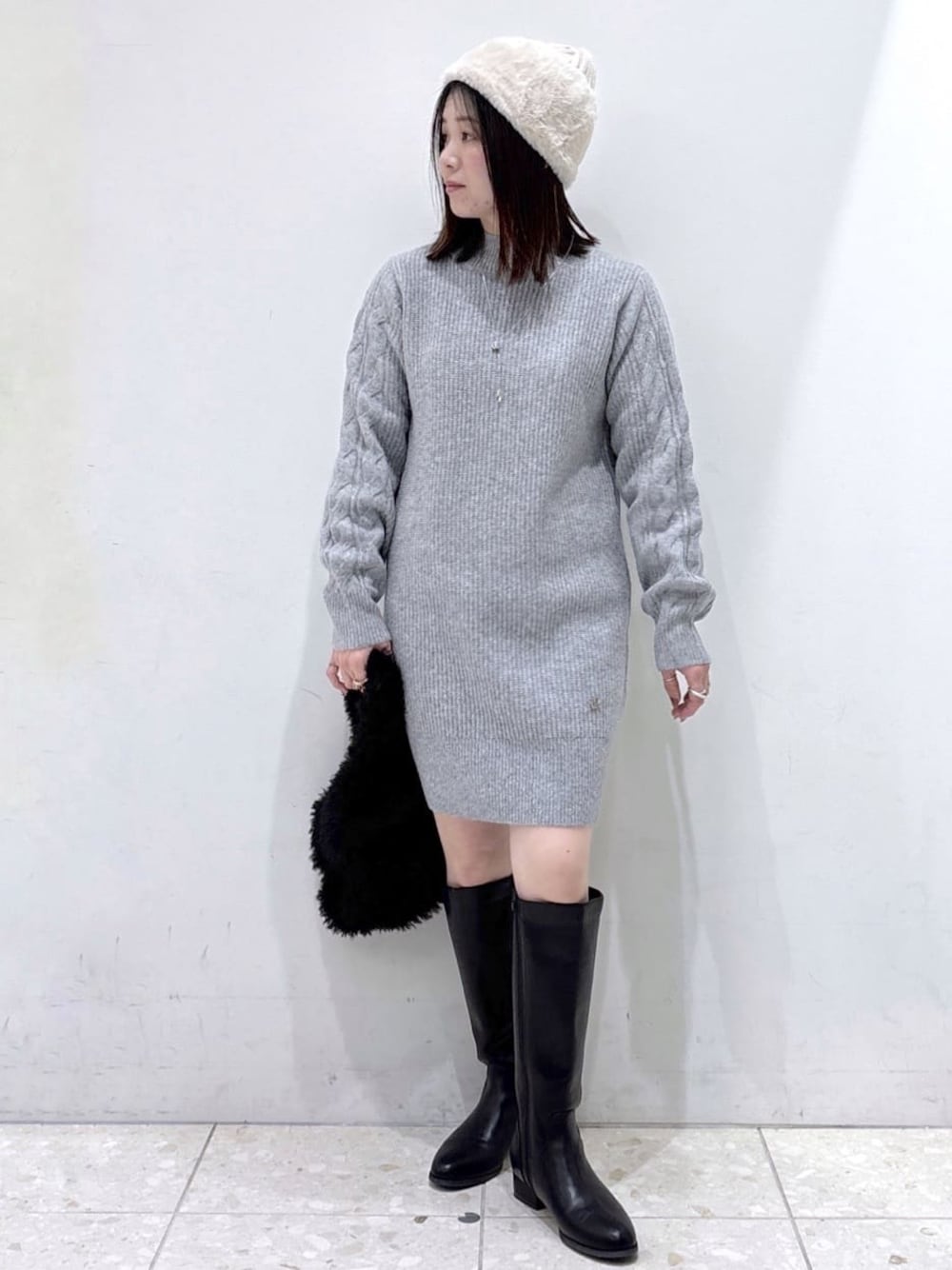 グレー系のワンピース、ブラック系のハンドバッグ、ブラック系のブーツを着用したレディースの冬コーディネートの1枚目の写真