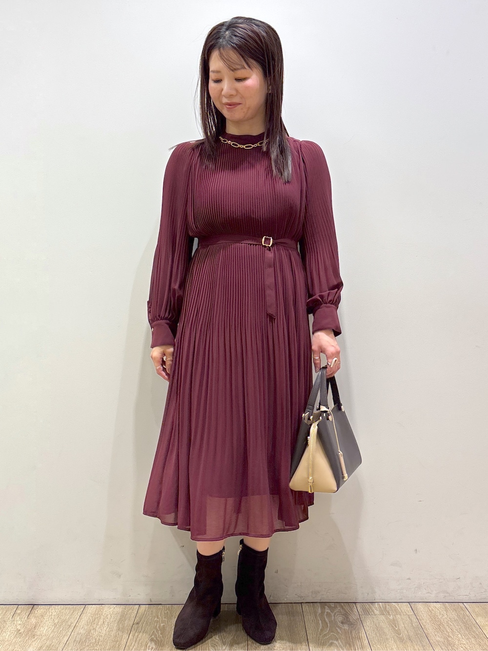 レッド系のワンピース、ブラウン系のボストンバッグ、ブラウン系のブーツを着用したレディースの秋コーディネートの1枚目の写真