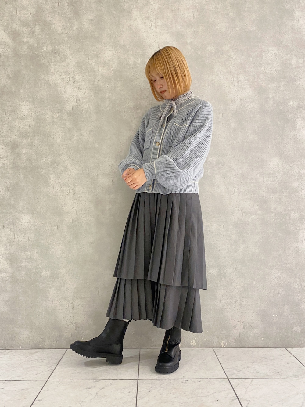 グレー系のスカート、ブルー系のカーディガン/ボレロ、グレー系のシャツ/ブラウスを着用したレディースの秋コーディネートの1枚目の写真