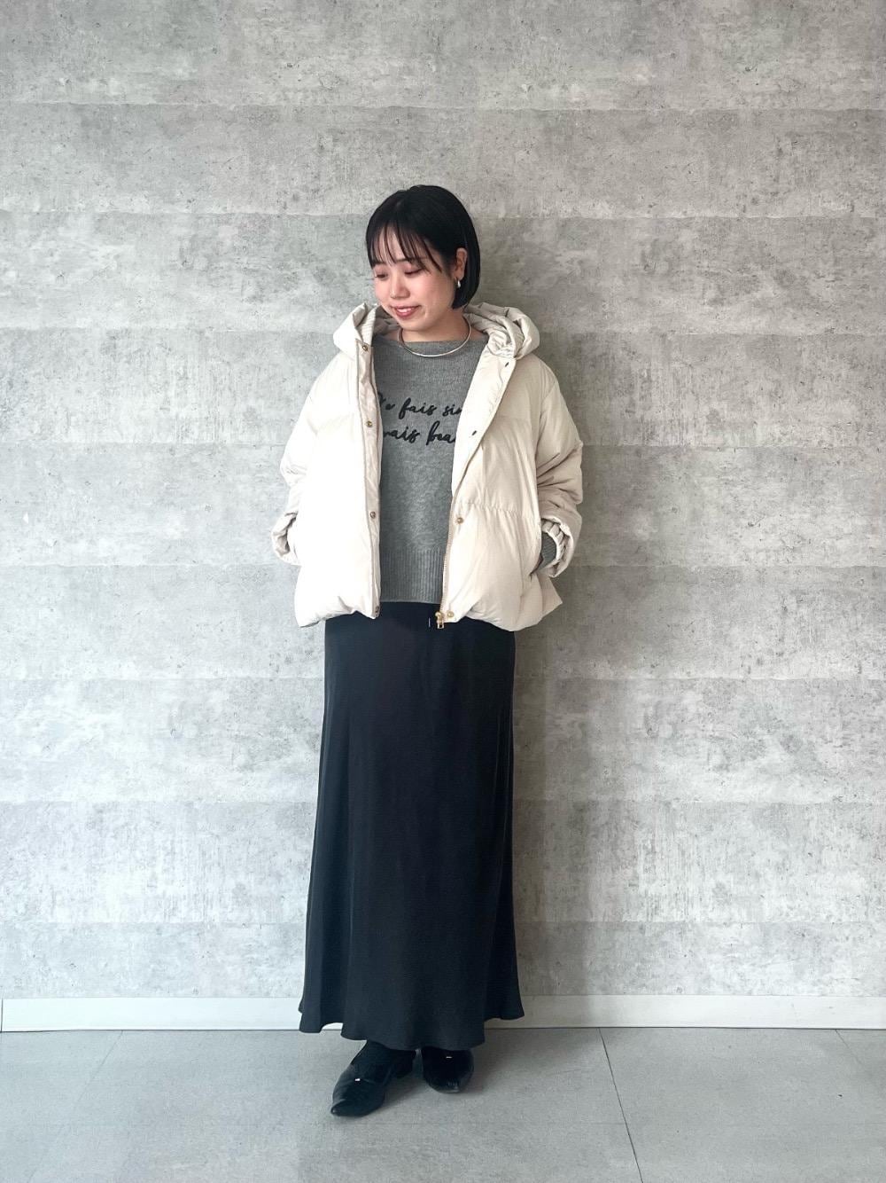 グレー系のスカート、ベージュ系のダウンジャケット/コート、グレー系のニット/セーターを着用したレディースの秋コーディネートの1枚目の写真