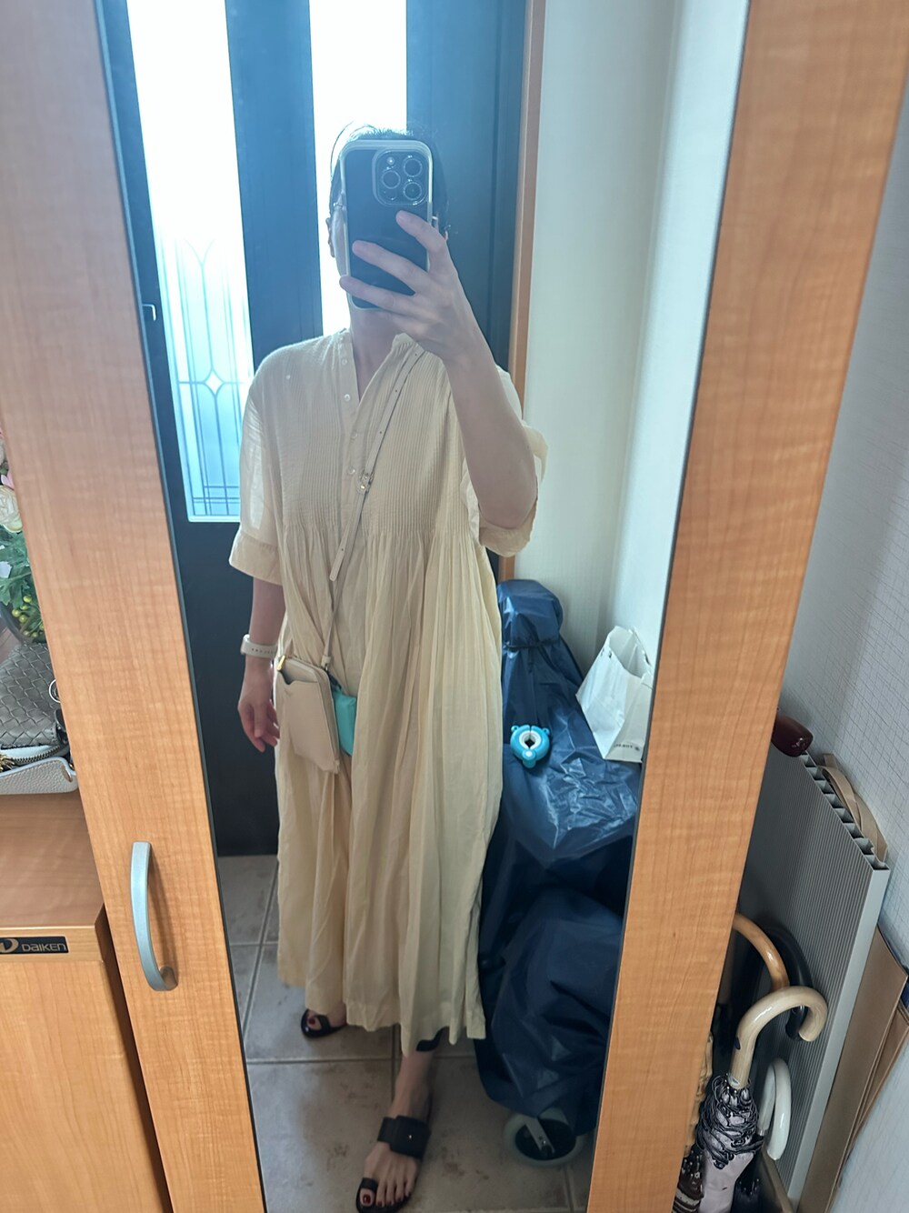 ベージュ系のワンピース、ブラック系のサンダル、ベージュ系のショルダーバッグを着用したレディースの夏コーディネートの1枚目の写真