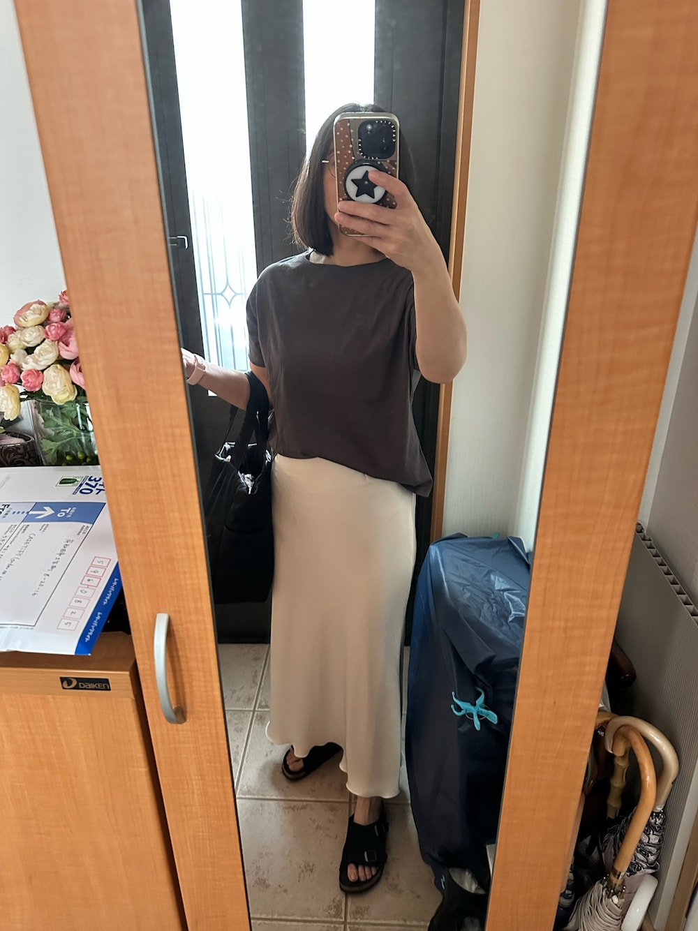 グレー系のTシャツ/カットソー、ホワイト系のスカート、ブラック系のサンダルを着用したレディースの秋コーディネートの1枚目の写真