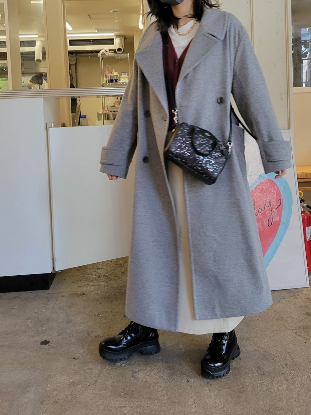 グレー系のチェスターコート、ホワイト系のスカート、ブラック系のブーツを着用したレディースの冬コーディネートの2枚目の写真