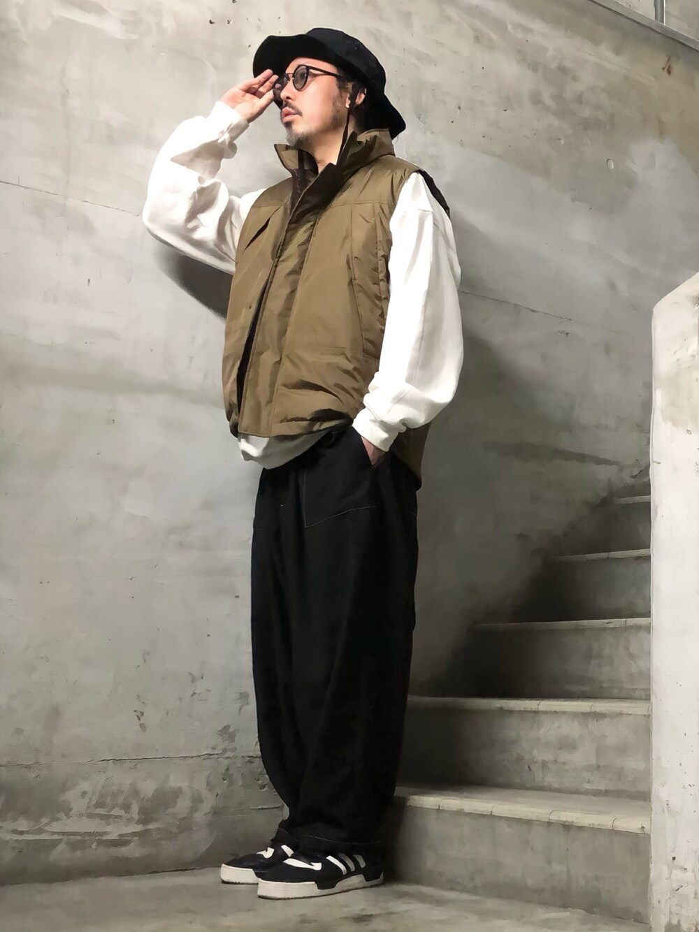 ブラウン系のダウンベスト、ホワイト系のスウェット、ブラック系のスニーカーを着用したメンズの秋コーディネートの1枚目の写真